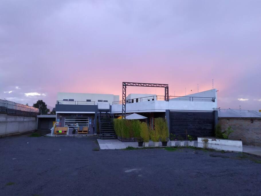 a building in a parking lot with a sunset in the background at Plaza Tababela near Quito Airport in Quito