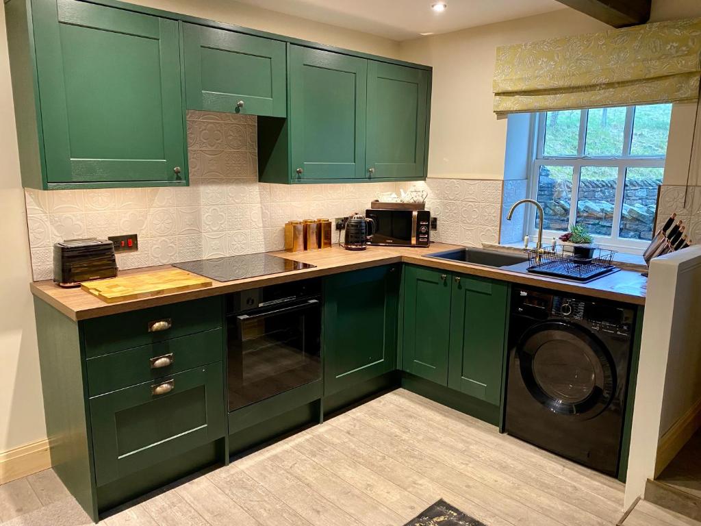 a green kitchen with a sink and a dishwasher at Cross Haw Cottage in Sedbergh