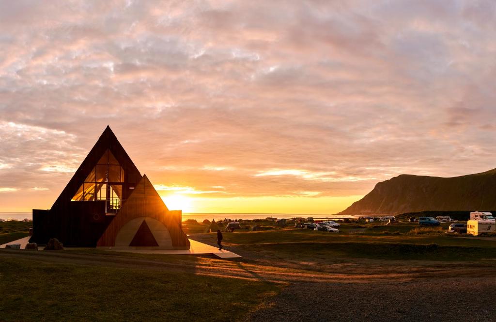 un pequeño edificio con una puesta de sol en el fondo en Lofoten Beach Camp en Ramberg