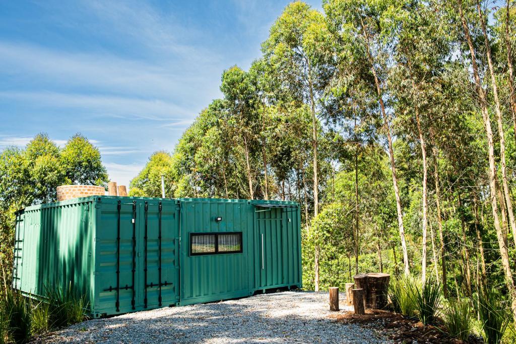 a green shed in the woods with trees in the background at Casa Container FIGO em meio a natureza na Serra Gaúcha in Flores da Cunha