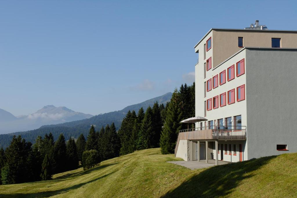 un bâtiment au sommet d'une colline herbeuse avec des arbres dans l'établissement Valbella-Lenzerheide Youth Hostel, à Lenzerheide