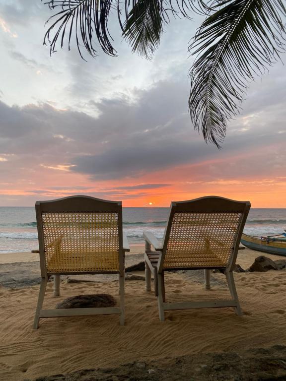 two chairs sitting on the beach at sunset at Kodi Beach Home in Galle