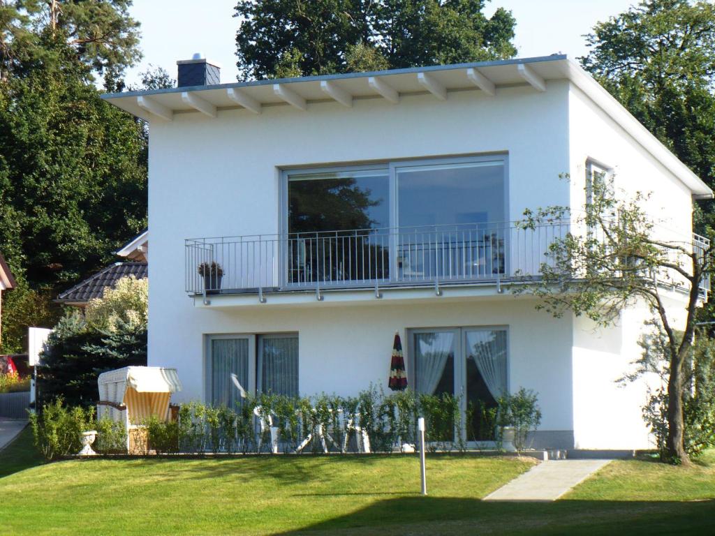 a white house with a balcony and a yard at Ferienwohnungen direkt am See bei den Kaiserbädern in Heringsdorf
