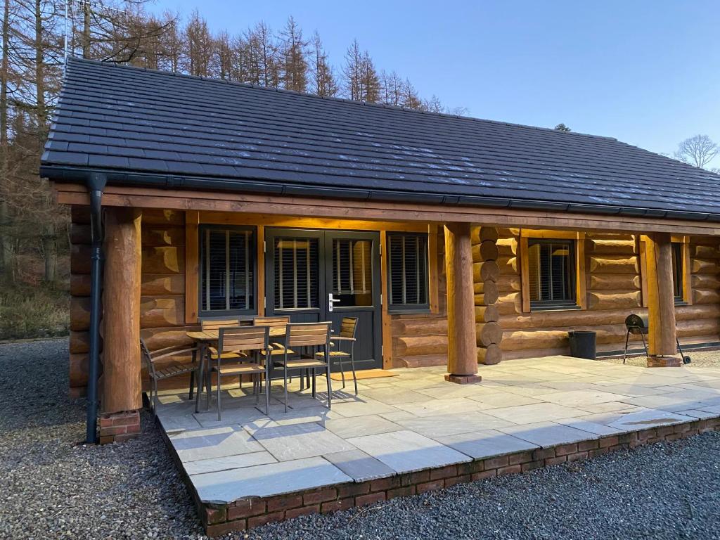 a log cabin with a table and chairs on a patio at Ewes Water Log Cabins in Langholm