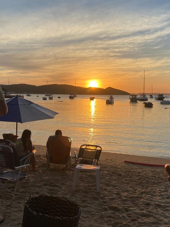 una pareja sentada en la playa viendo la puesta de sol en Tortuguita Ossos - Suítes en Búzios