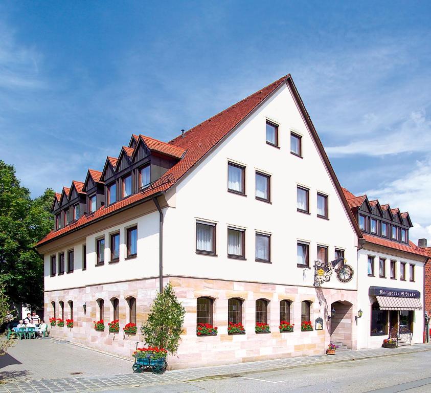 un grand bâtiment blanc avec un toit rouge dans l'établissement BLÖDEL Gasthof Grüner Baum, à Nuremberg