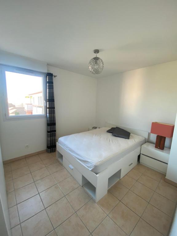 ein weißes Schlafzimmer mit einem Bett und einem Fenster in der Unterkunft Appartement moderne en résidence avec piscine in Mèze