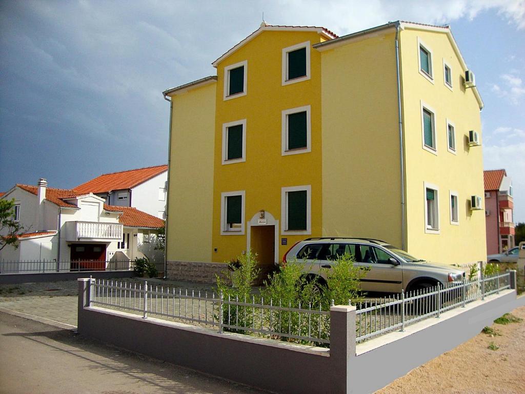 une maison jaune avec une voiture garée devant elle dans l'établissement Apartments Marina, à Vodice