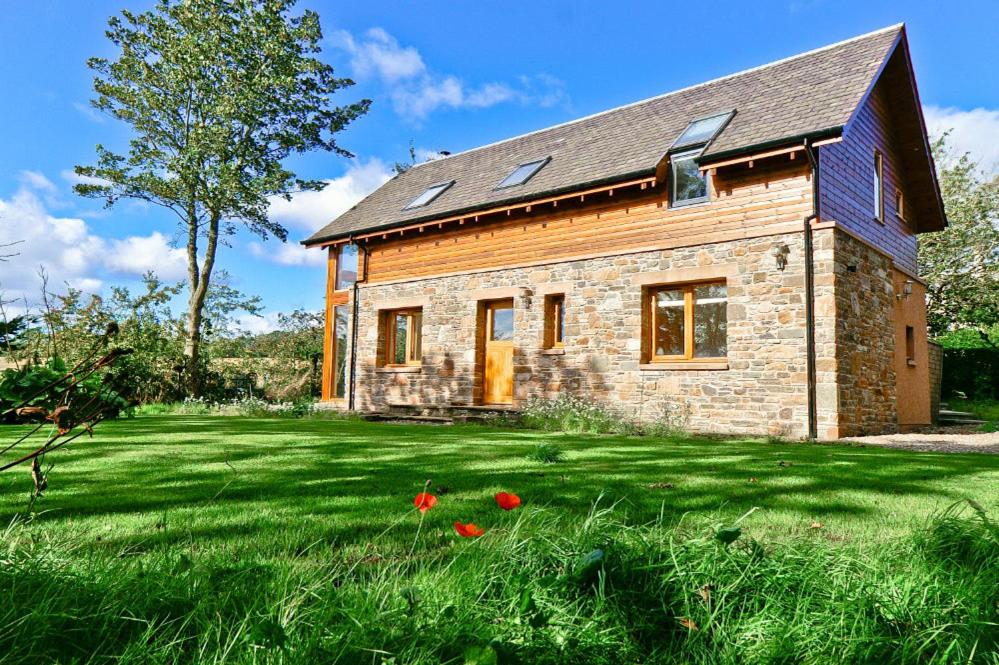 une maison en pierre avec des fleurs rouges dans l'herbe dans l'établissement Anglers Retreat, à Brechin