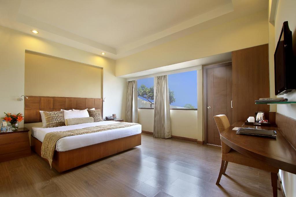 a bedroom with a bed and a desk and a window at Hotel Express Towers in Vadodara
