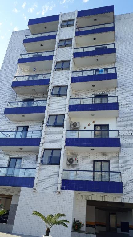 un edificio de apartamentos alto con ventanas azules y una palmera en Studio novo - Vai te surpreender, en Praia Grande