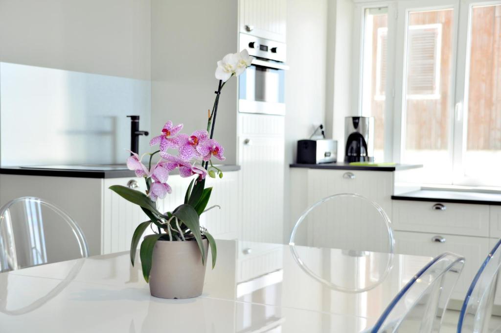 a white kitchen with a table with a vase with flowers at Résidence La Plage d'Or in Vierville-sur-Mer