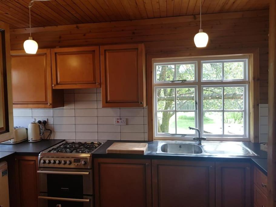 a kitchen with a stove and a sink and two windows at Pine Cabin, Strathyre. A cosy escape from it all. in Strathyre