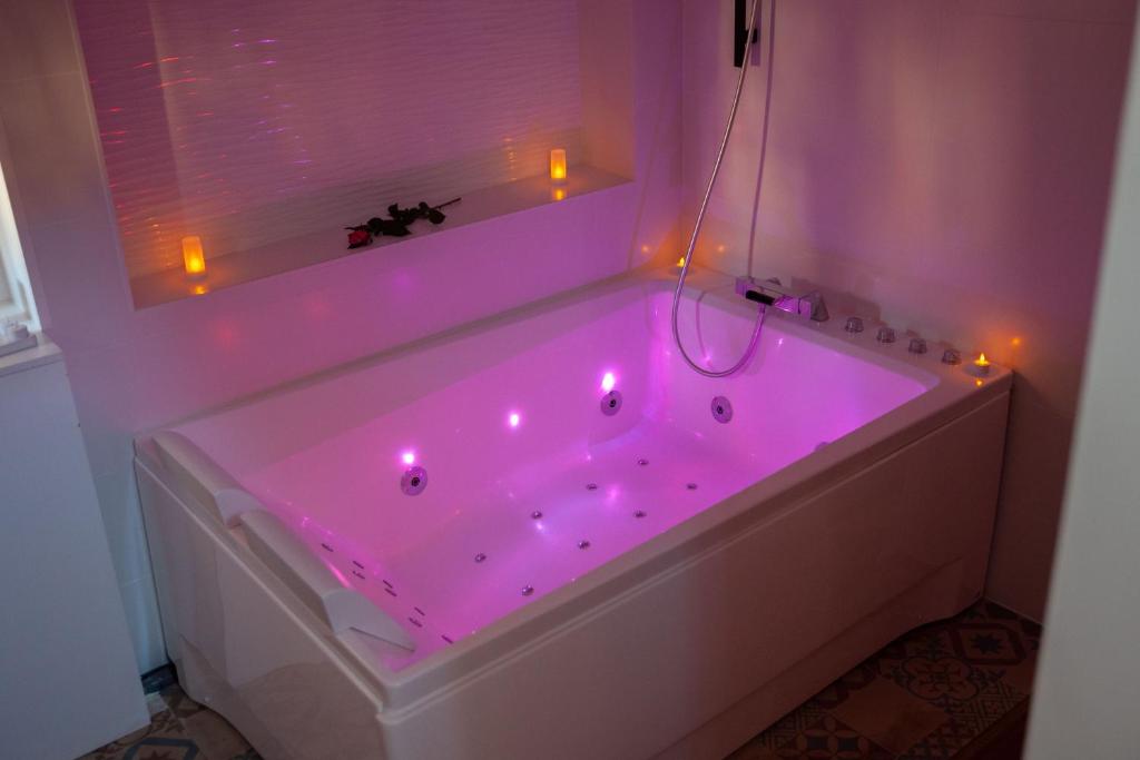 a bathroom with a tub lit up with pink lights at Suite 50 Nuances avec Jacuzzi Privatif Dark Room Perpignan in Villeneuve-de-la-Raho