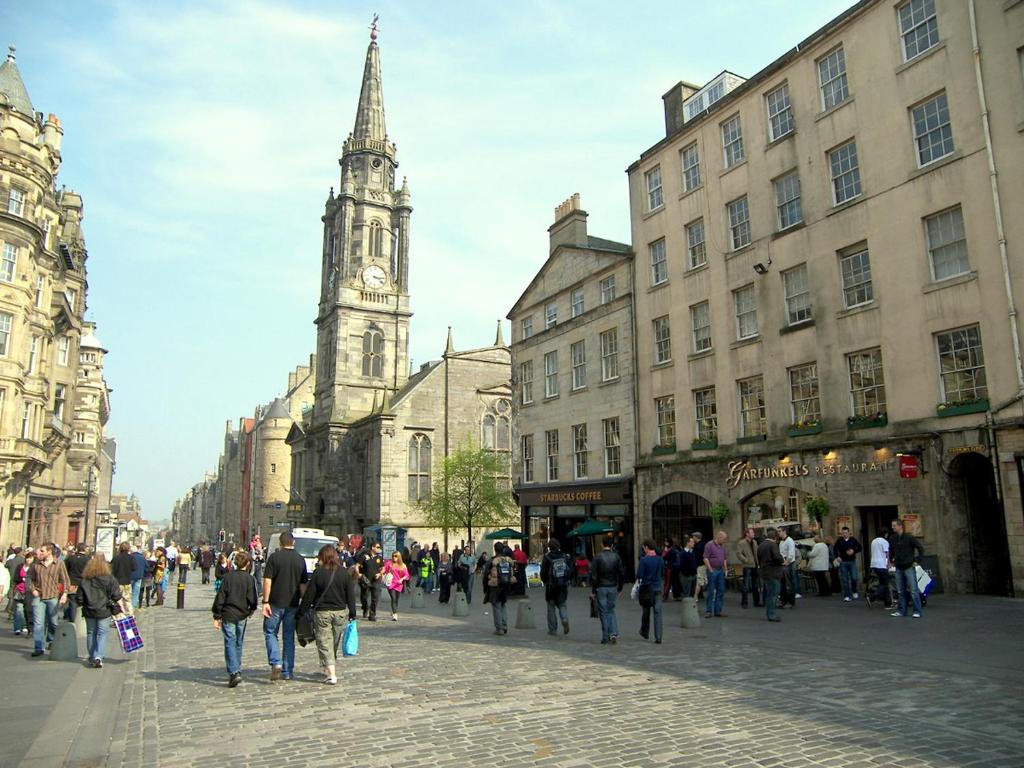 un grupo de personas caminando por una calle con una torre del reloj en Royal Mile Apartment, en Edimburgo