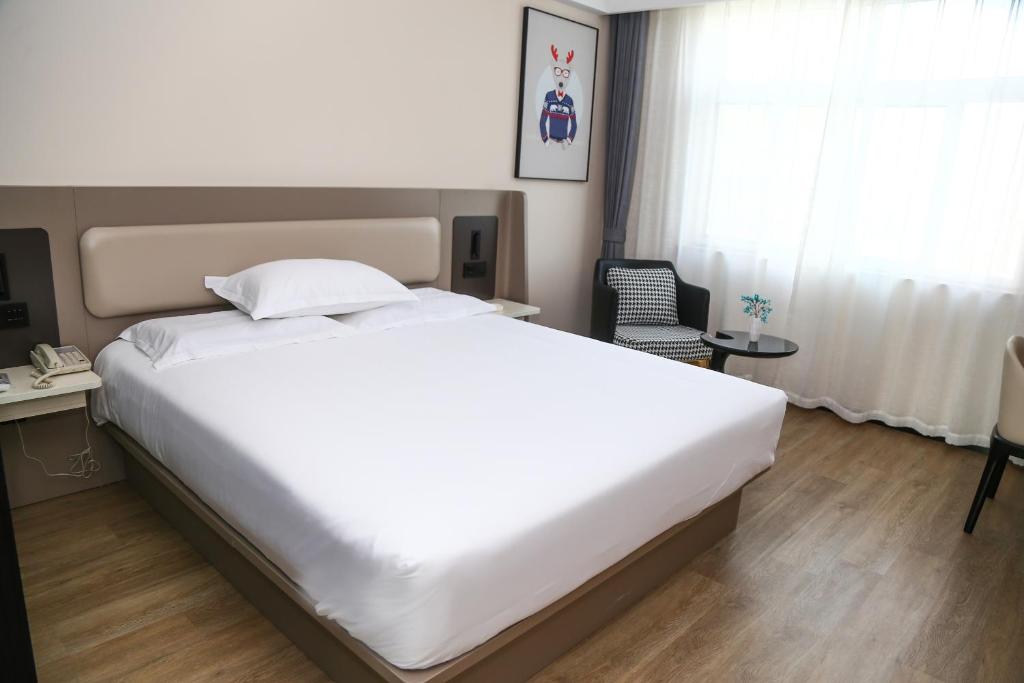 um quarto com uma grande cama branca e uma cadeira em 银座佳驿（潍坊寒亭高铁北站店） em Weifang