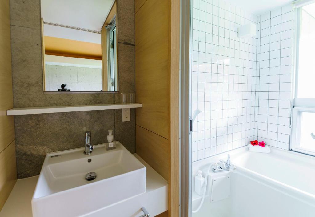 a bathroom with a sink and a tub and a mirror at Asahinoyado Shidakaji in Nanjo