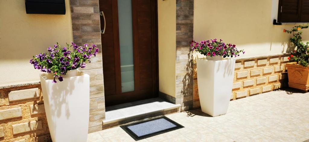 Perla del Sud - Guest House في لامبيدوسا: مزهريتين بيض مع زهور أرجوانية على جانب الباب