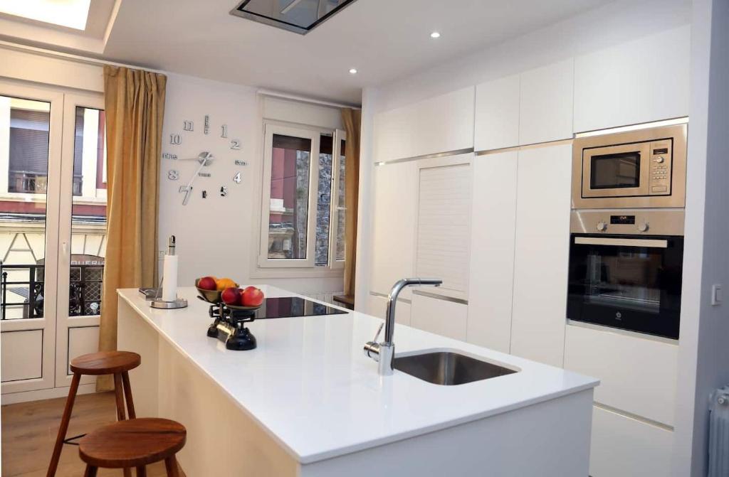 a white kitchen with a sink and two stools at Piso Reformado a 2 Min del Casco Viejo Con Garaje Gratis in Bilbao