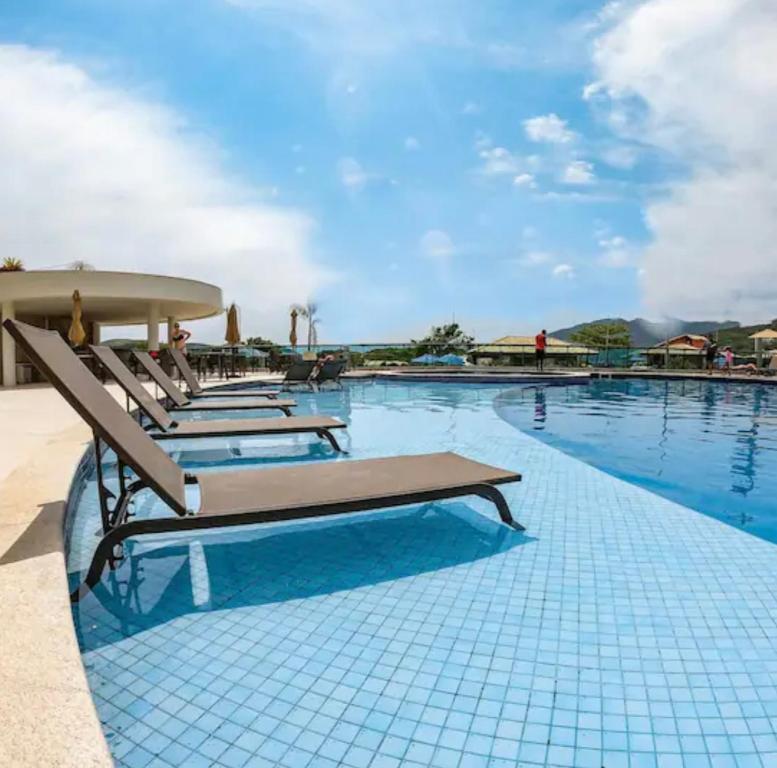 a pool with chaise lounge chairs on the side at Apto paraíso praia dos anjos in Arraial do Cabo