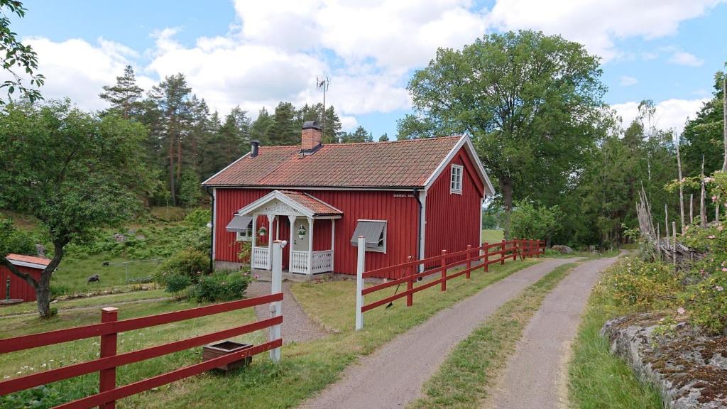 un granero rojo con una valla al lado de un camino de tierra en Året runt i väldigt härlig natur Bo på lantgård en Rimforsa
