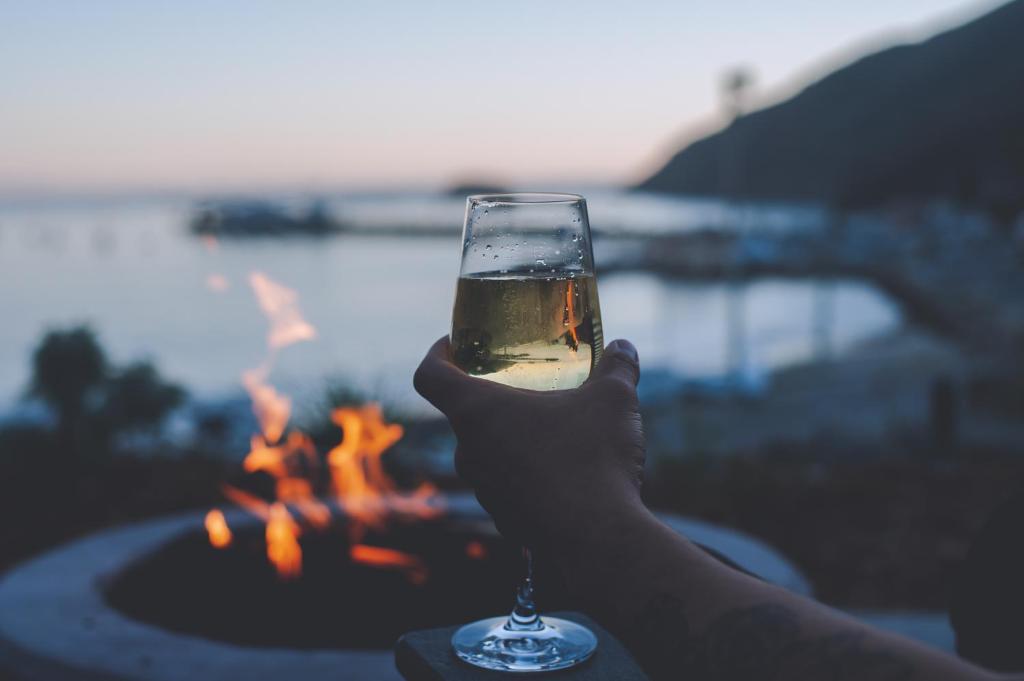 a person holding a glass of wine in front of a fire at Flying Flags Avila Beach in Avila Beach