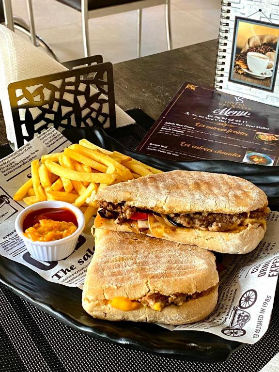 a sandwich and french fries on a tray with a sandwich and sauce at Hotel VELSATIS in Beni Mellal