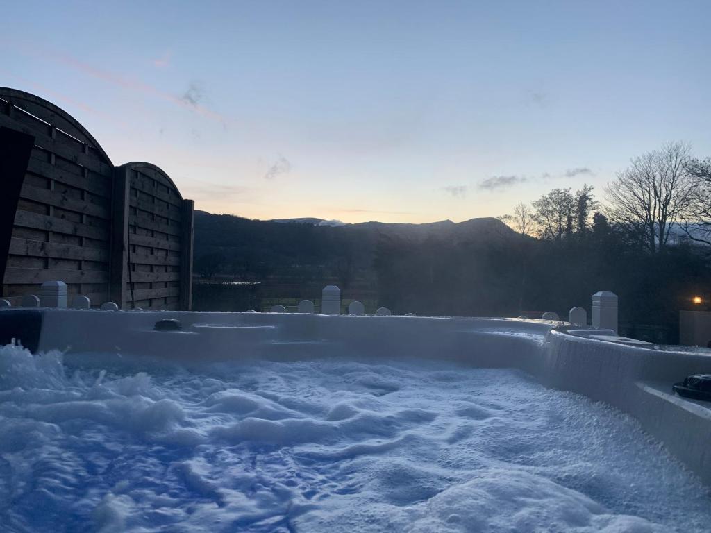 einen schneebedeckten Whirlpool neben Gebäuden in der Unterkunft Semi Detached Cottage Snowdonia with hot tub in Tal-y-Cafn