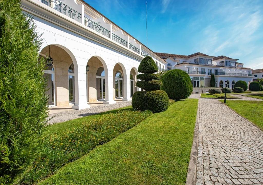 a large white building with a pathway and bushes at Montebelo Principe Perfeito Viseu Garden Hotel in Viseu