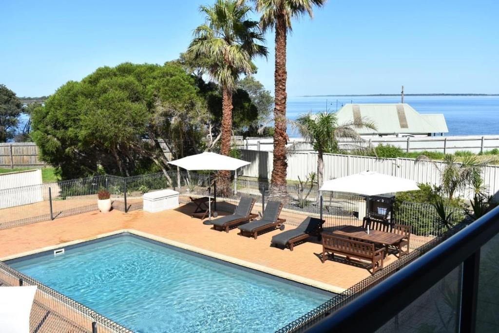 a swimming pool with chairs and umbrellas on a balcony at Metung Waters Motel and Apartments in Metung