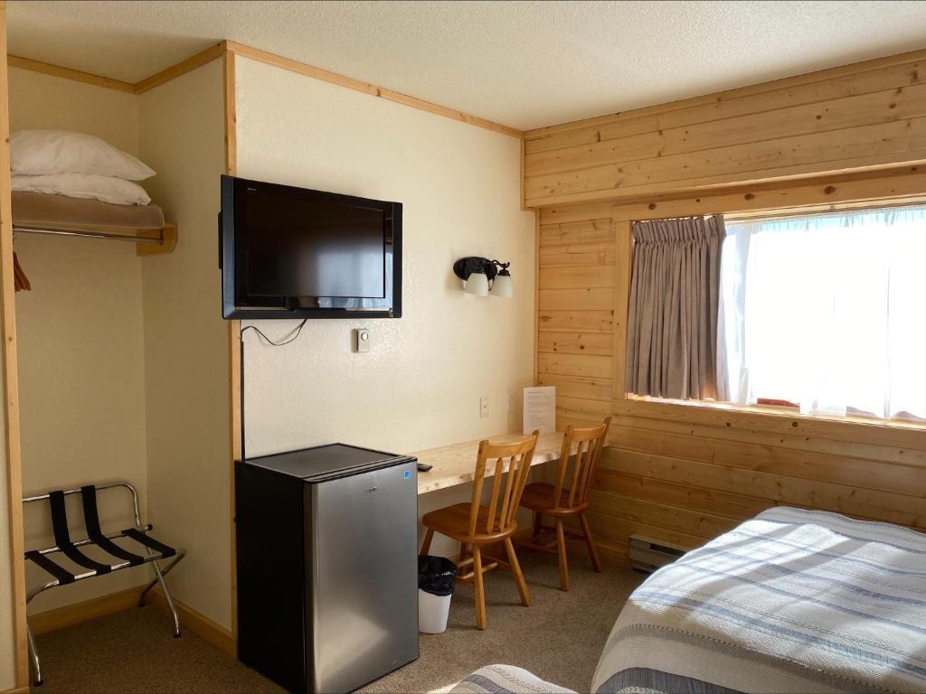een kamer met een bed, een bureau en een televisie bij Stork Nest Inn in Smithers