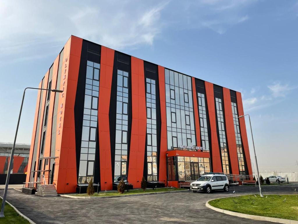 a large red building with a car parked in a parking lot at Olympic Hotel in Türkistan