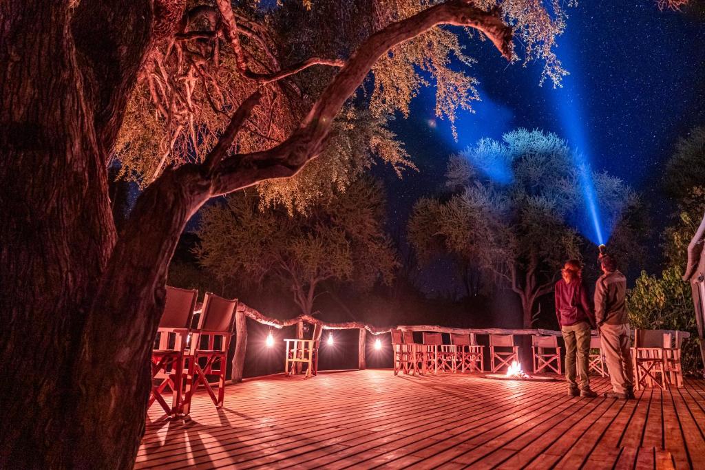 O Bona Moremi Safari Lodge في Khwai: شخصان يقفان على سطح السفينة تحت شجرة في الليل