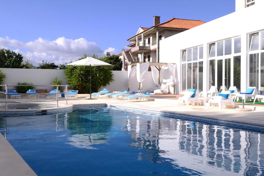 uma piscina com cadeiras azuis e um edifício em Hotel Dom Nuno em Santiago do Cacém