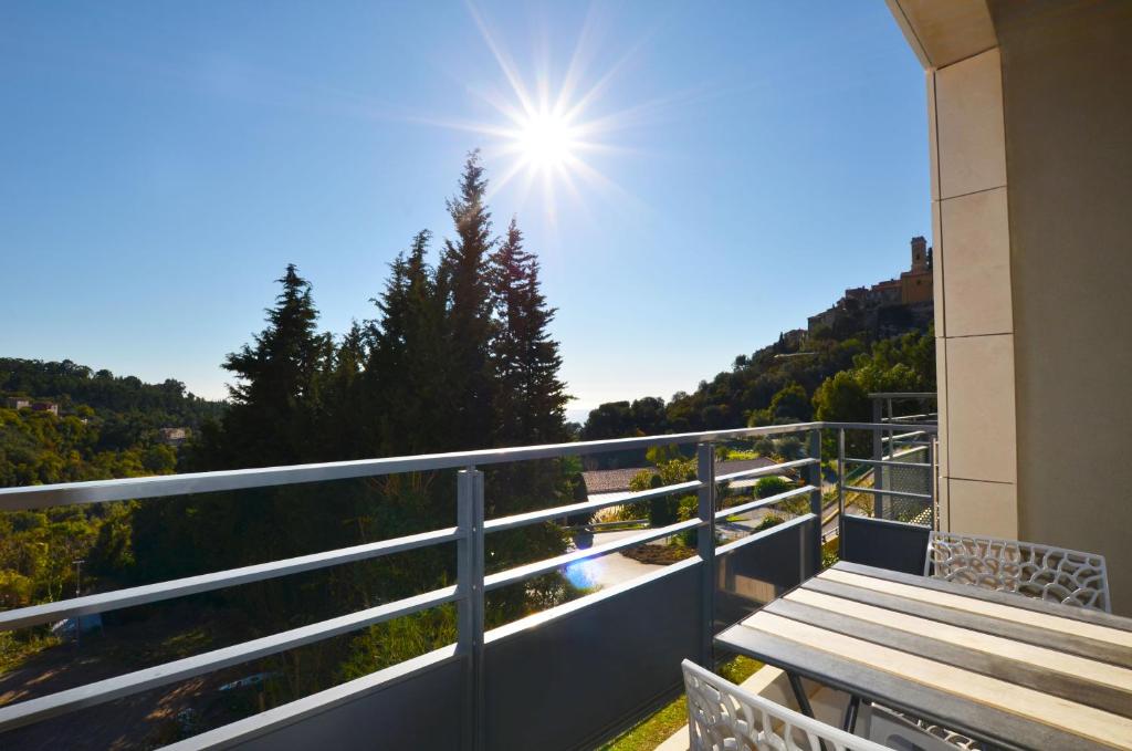 a balcony with a wooden table and the sun in the sky at La Perle d'Eze - Aparthotel in Éze