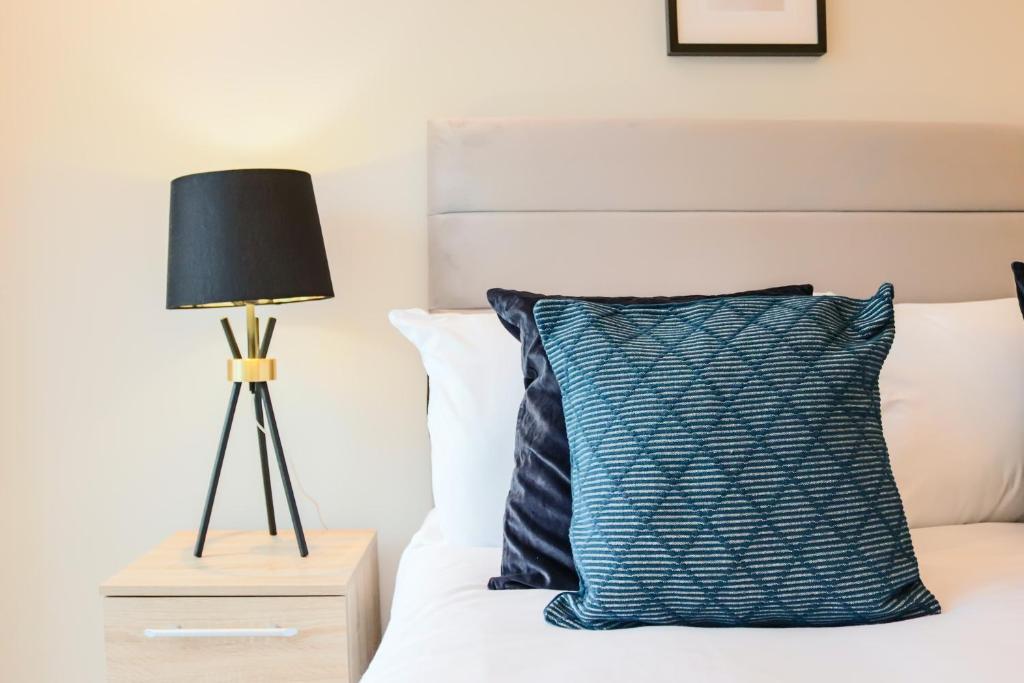 a bed with a blue pillow and a lamp at Portfolio Apartments - Welwyn Town Centre in Welwyn Garden City