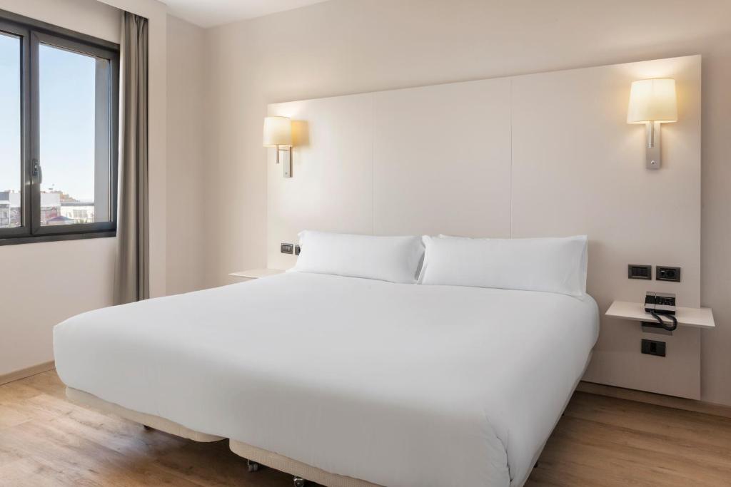a white bedroom with a large white bed and a window at B&B HOTEL Elche in Elche