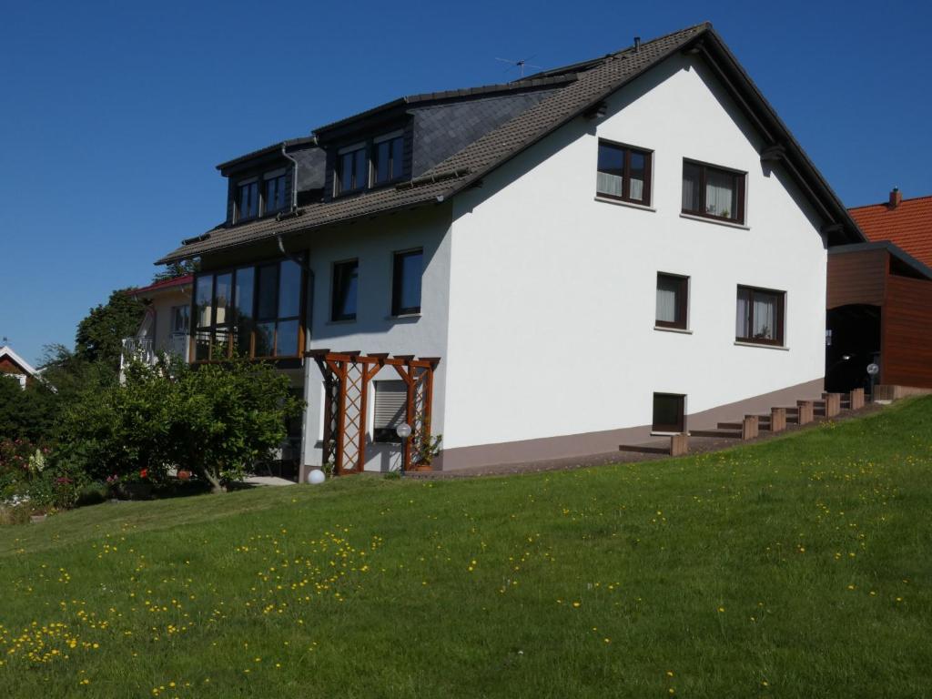 a white house with a black roof on a green lawn at Ferienwohnung Neumann in Gersfeld