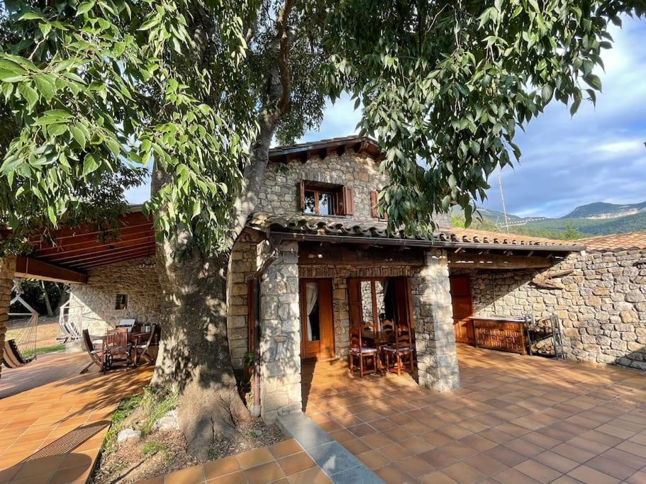 una casa de piedra con un árbol delante en El Vilarot. La casa de piedra en la naturaleza., en Girona