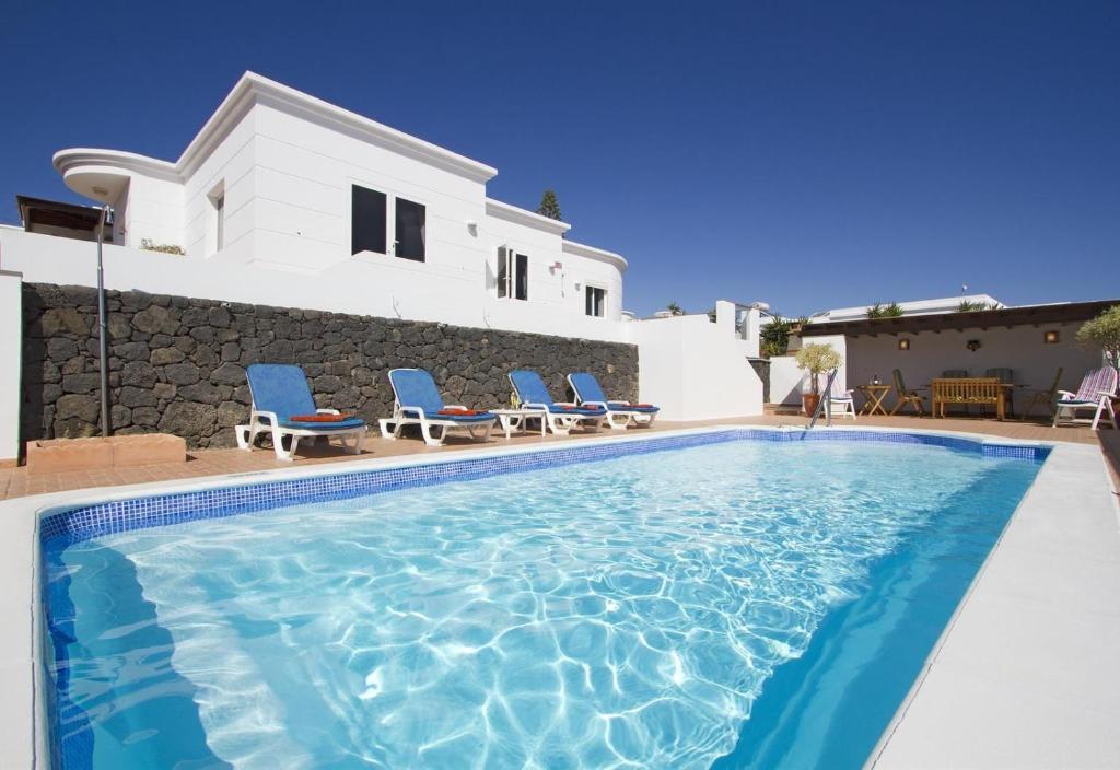 une piscine avec des chaises et une maison en arrière-plan dans l'établissement Casa Mcelroy, à Tías