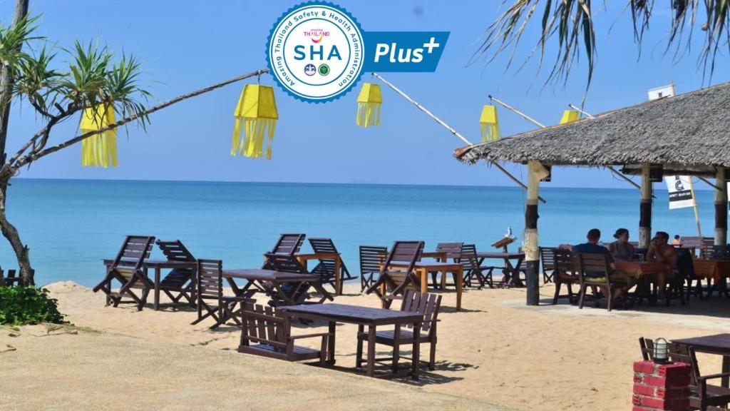 a beach with chairs, tables and umbrellas at Lanta Nice Beach Resort - SHA Extra Plus in Ko Lanta