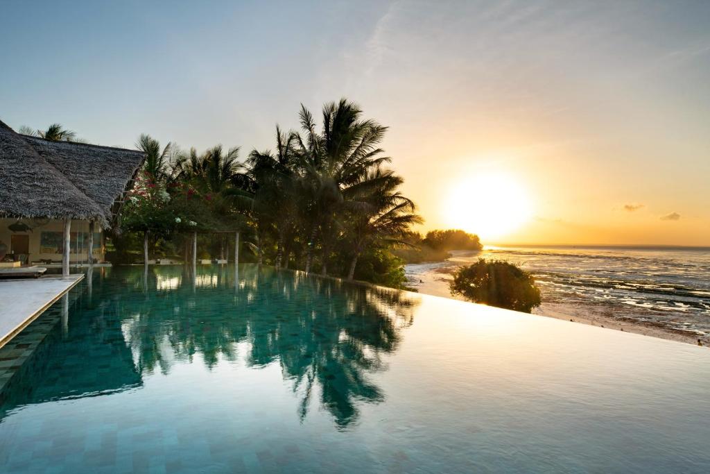 una piscina junto a una playa con puesta de sol en Qambani Luxury Resort, en Michamvi