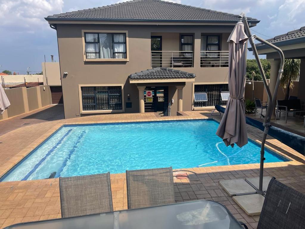 a swimming pool with an umbrella in front of a house at Thokomala Guest House in Germiston