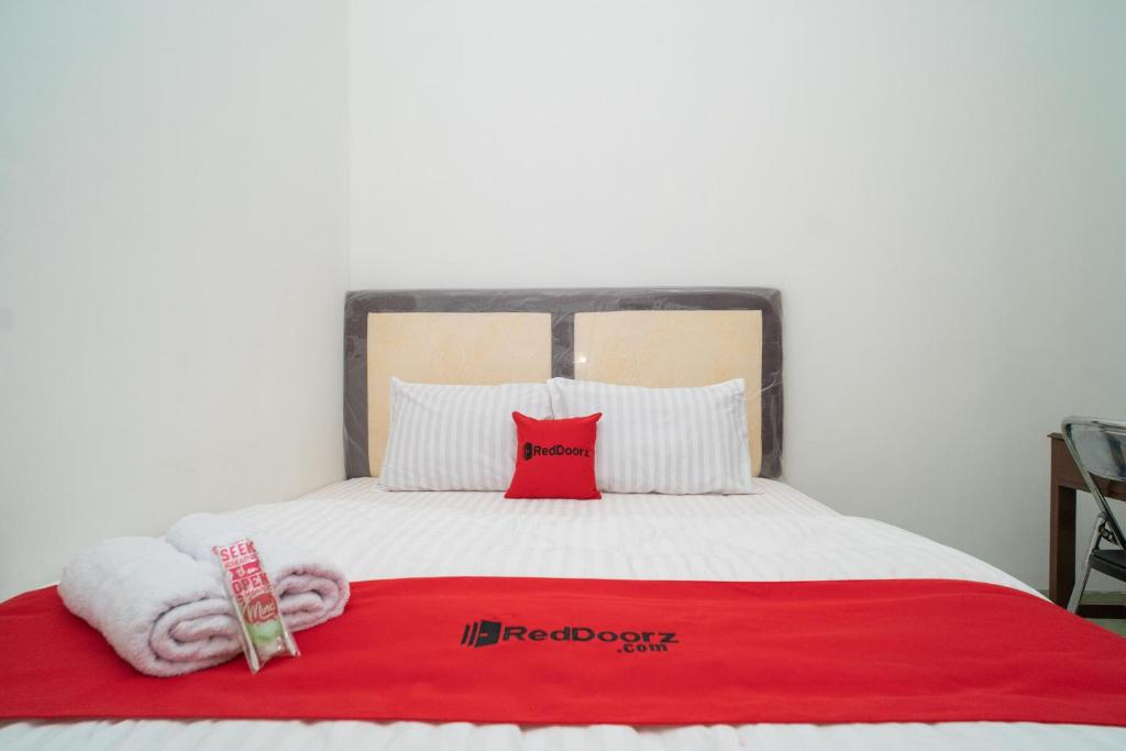 a bed with a red blanket and two pillows on it at RedDoorz near Bundaran Ciceri in Kumprung