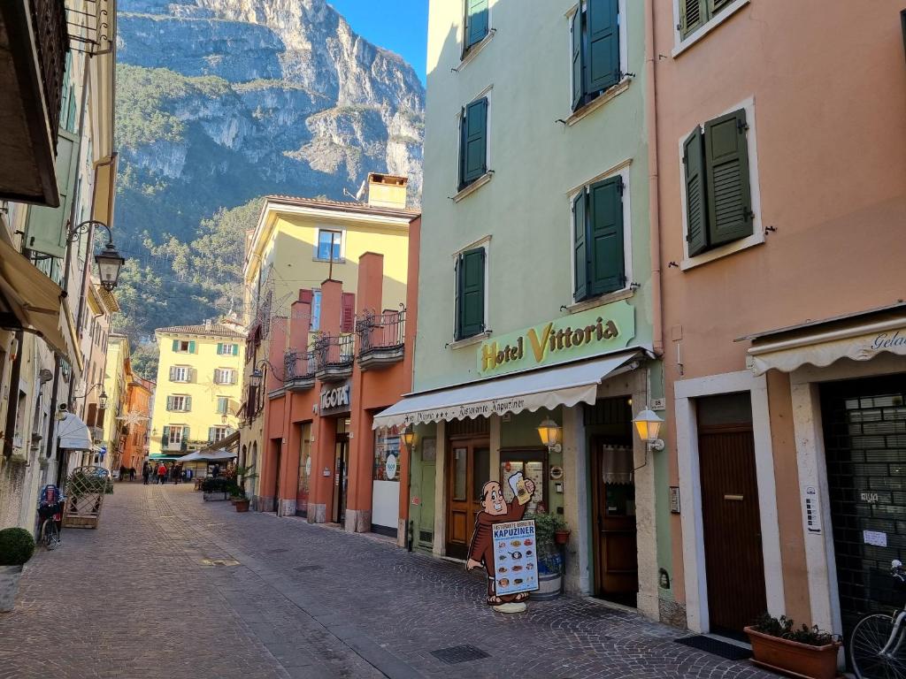 a street with buildings and a mountain in the background at Hotel Vittoria in Riva del Garda