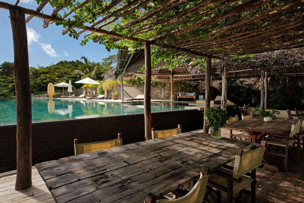 a wooden table and chairs next to a swimming pool at Qambani Luxury Resort in Michamvi