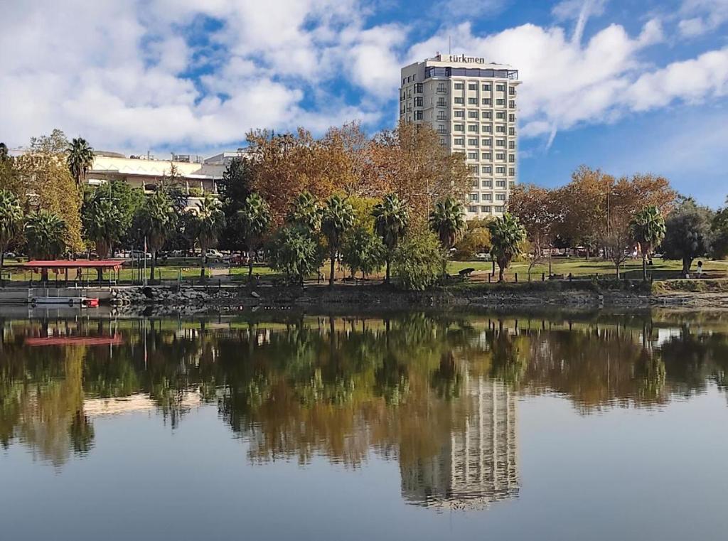 Türkmen Riverside Hotel Adana في أضنة: مبنى طويل بجوار بحيرة مع مبنى