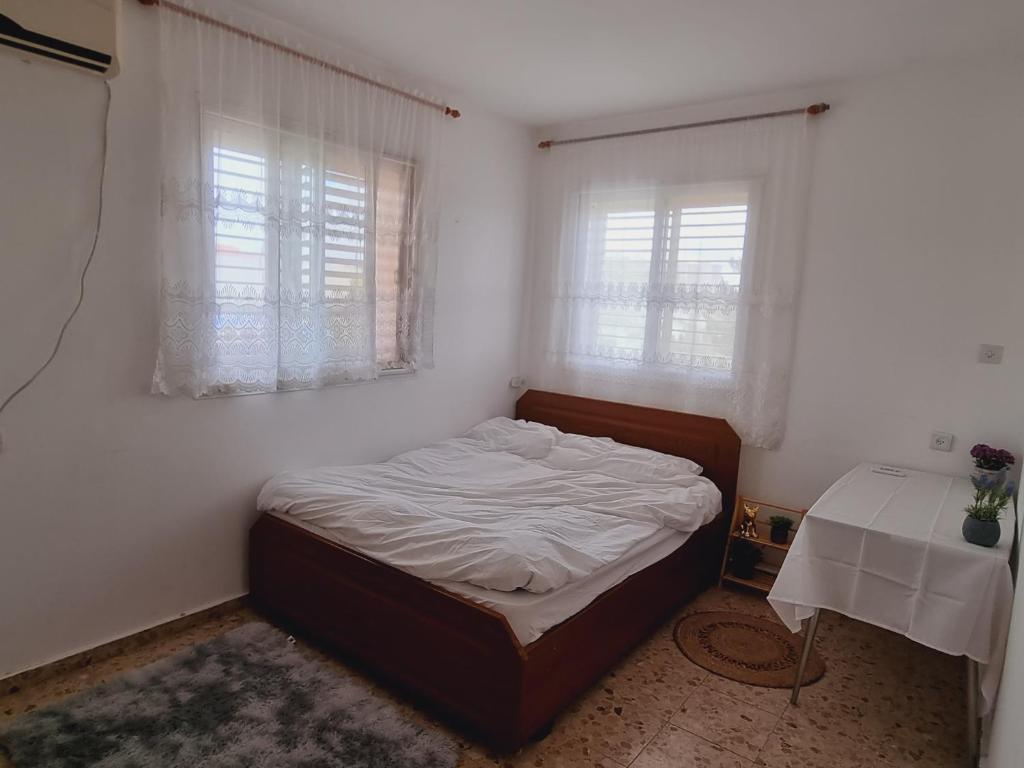 Cama en habitación con mesa y 2 ventanas en נווה מדבר - אירוח מקומי, en Arad