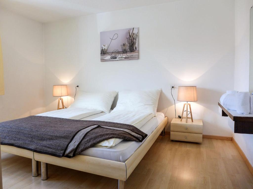 a bedroom with a bed with white walls and two lamps at Apartment Chesa Ova Cotschna 305 by Interhome in St. Moritz