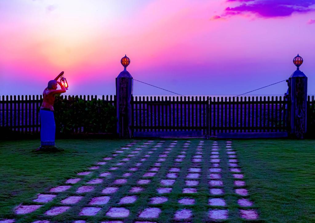 Iranawila的住宿－Calypso Sunset，站在围栏旁的女人,一边欣赏日落
